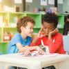 Row of multiethnic elementary students reading book in classroom